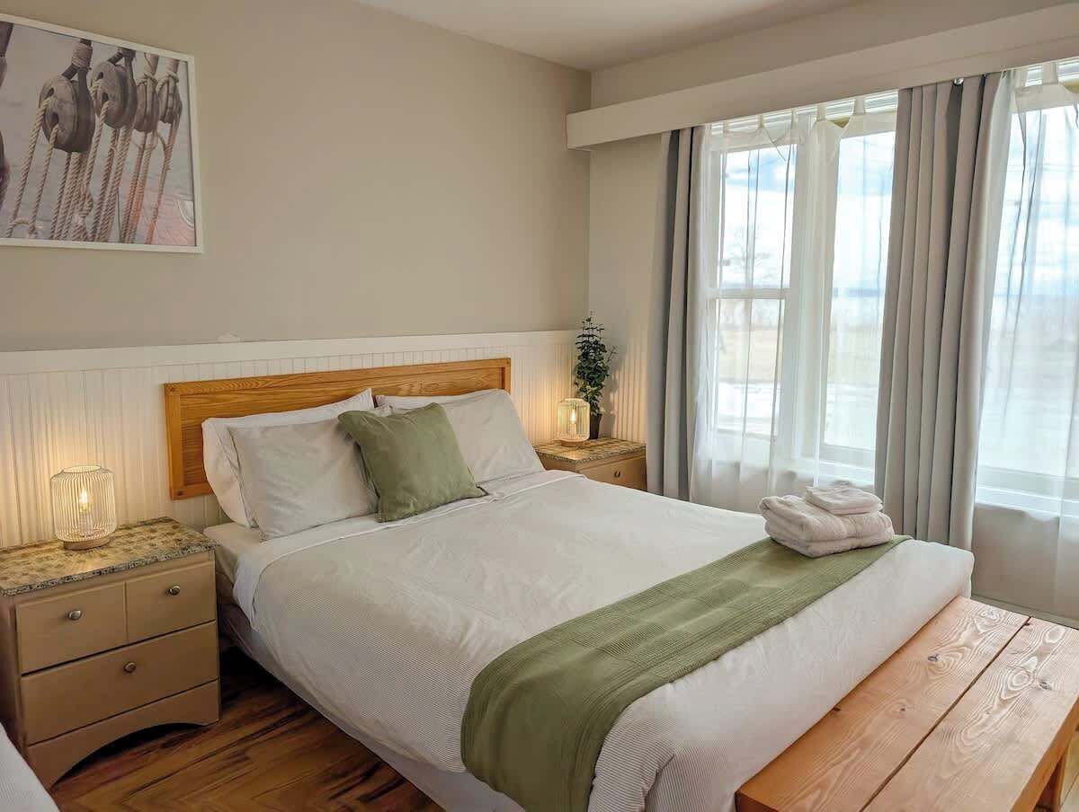 Una cama bien hecha con cabecera de madera, una lámpara de noche y una ventana con cortinas.