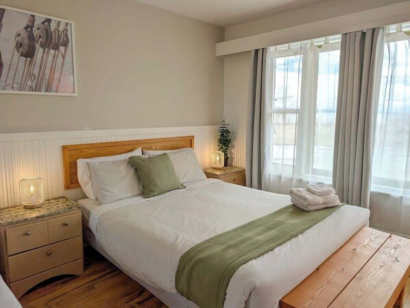 A neatly made bed with a wooden headboard, a bedside lamp, and a window with curtains.