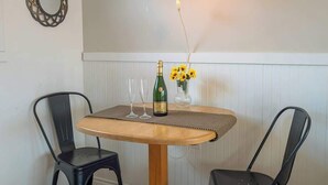 A dining area with a round wooden table, two black chairs, a bottle of champagne, and a vase with sunflowers.