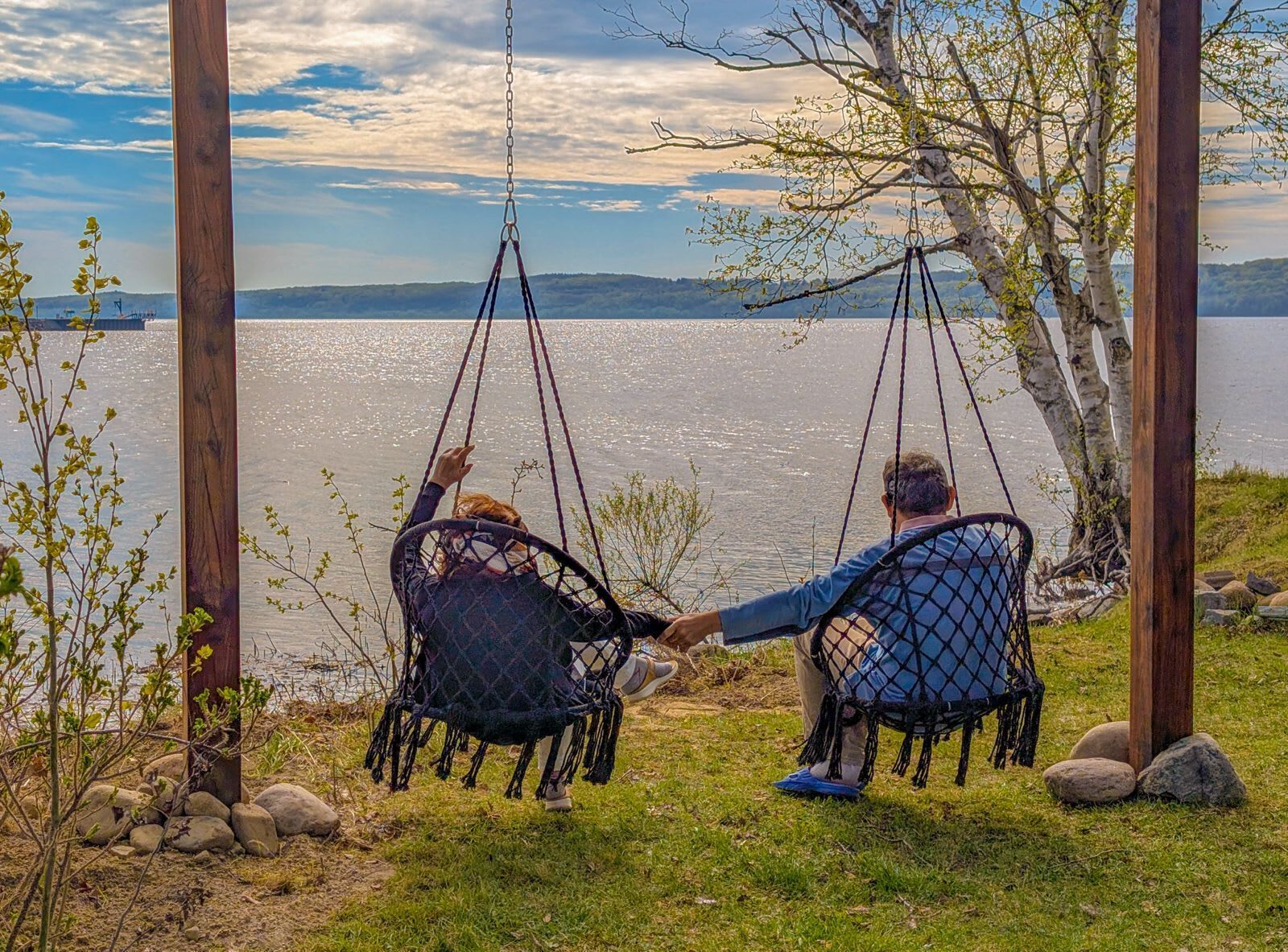 Dos personas sentadas en columpios con vista a un lago bajo un cielo despejado.