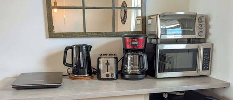 A compact kitchenette with a coffee maker, toaster, microwave, and a laptop on the counter.