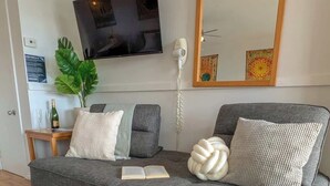 Una sala de estar moderna con un sofá gris, un espejo grande, un televisor montado en la pared y una planta.