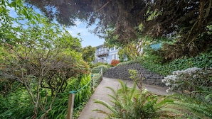 A pathway leading to a house surrounded by lush greenery and a stone wall. - Sunset Point - Coos Bay, OR (Coos Bay)