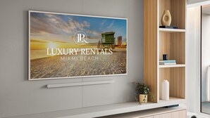 Et vægmonteret fjernsyn, der viser 'LUXURY RENTALS MIAMI BEACH' med et strandbillede.