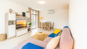 Ein modernes Wohnzimmer mit Flachbildfernseher, einer Couch, einem Esstisch und Stühlen.