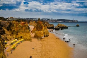 Ein Strand mit großen Felsformationen, sandigem Ufer und einer Reihe von Sonnenschirmen.