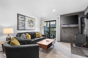 A modern living room with a black leather sofa, a wooden coffee table, and a fireplace. - Relaxed 1BR Mountain Escape | Fireplace & Parking (Steamboat Springs)