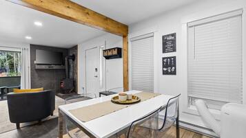 A modern kitchen with a white countertop, a black sofa, and a dining table with chairs.