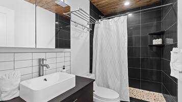 A modern bathroom with a white sink, dark wooden vanity, a toilet, and a shower with a white curtain.