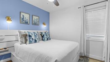 A bedroom with a bed, a ceiling fan, wall-mounted lights, and a window with blinds.