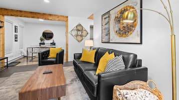 A modern living room with a black leather sofa, wooden coffee table, and a large abstract painting.