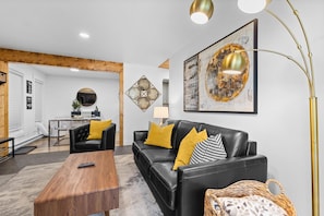 A modern living room with a black leather sofa, wooden coffee table, and a large abstract painting. - Relaxed 1BR Mountain Escape | Fireplace & Parking (Steamboat Springs)