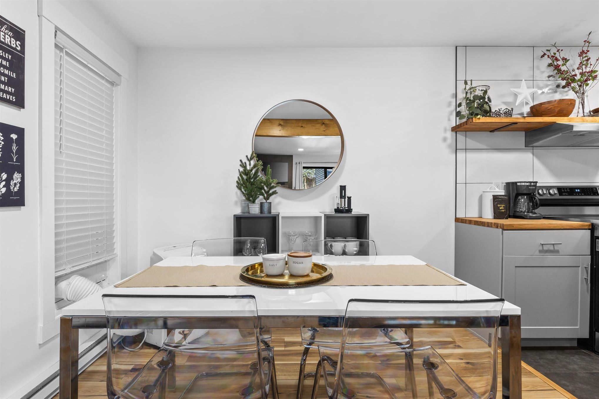 A modern kitchen with a dining table, chairs, a round mirror, and a coffee station.