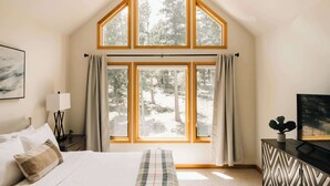 A bedroom with a large window, a bed, a bedside table, a lamp, and a painting. - Peaceful Getaway with Hot Tub | Views | Evergreen (Evergreen)