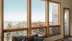 A room with large windows, a wooden deck, and a brown leather couch. - Peaceful Getaway with Hot Tub | Views | Evergreen (Evergreen)