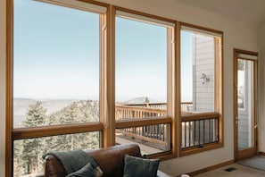 A room with large windows, a wooden deck, and a brown leather couch. - Peaceful Getaway with Hot Tub - Views - Evergreen (Evergreen)