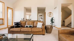 A spacious living room with a leather sofa, a glass coffee table, and a wooden side table. - Peaceful Getaway with Hot Tub | Views | Evergreen (Evergreen)
