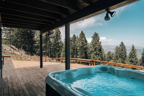 Un jacuzzi en una terraza de madera con vistas a un bosque y montañas.