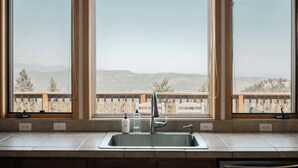 A kitchen with a large window, a sink, and a wooden deck. - Peaceful Getaway with Hot Tub | Views | Evergreen (Evergreen)