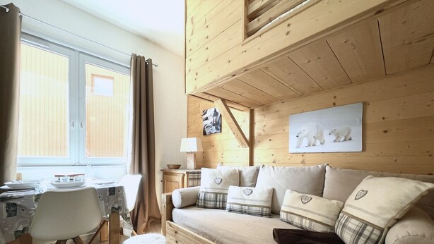 A cozy wooden cabin interior with a dining area, a sofa with decorative pillows, and a polar bear artwork on the wall. - (4.13) Studio cosy skis aux pieds 3 vallées (Les Menuires)