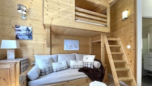 A cozy wooden room with a bunk bed, a small stool, a ladder, and a nightstand with a lamp. - (4.13) Studio cosy skis aux pieds 3 vallées (Les Menuires)