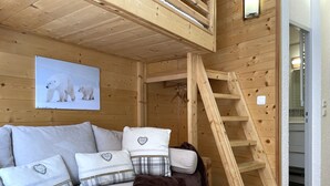 A wooden cabin interior with a sofa, pillows, a blanket, and a ladder. - (4.13) Studio cosy skis aux pieds 3 vallées (Les Menuires)