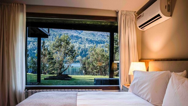 Ein Hotelzimmer mit einem großen Bett, Blick auf See und Wald, und einer Klimaanlage.