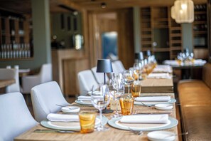 A restaurant with long tables set for dining, a bar area in the background, and a modern interior design. - Auria Angostura (Villa La Angostura)