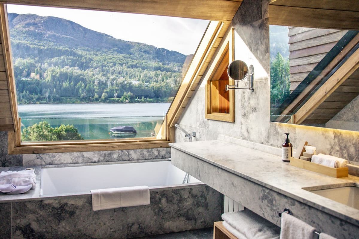 A bathroom with a bathtub, a sink, a mirror, and a view of a lake and forest.