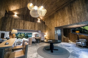 A spacious indoor area with a high ceiling, wooden paneling, a round table, and seating arrangements. - Auria Angostura (Villa La Angostura)