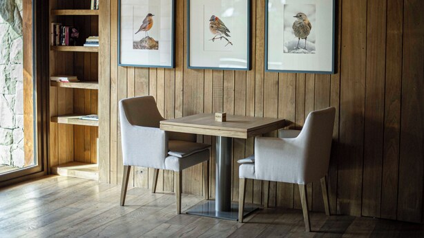 A wooden-paneled wall with three framed bird pictures, a wooden table with two chairs, and a bookshelf with books and decorative items. - Auria Angostura (Villa La Angostura)