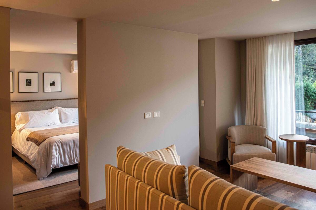 A hotel room with a bed, a sofa, a chair, a small table, and a window with curtains.