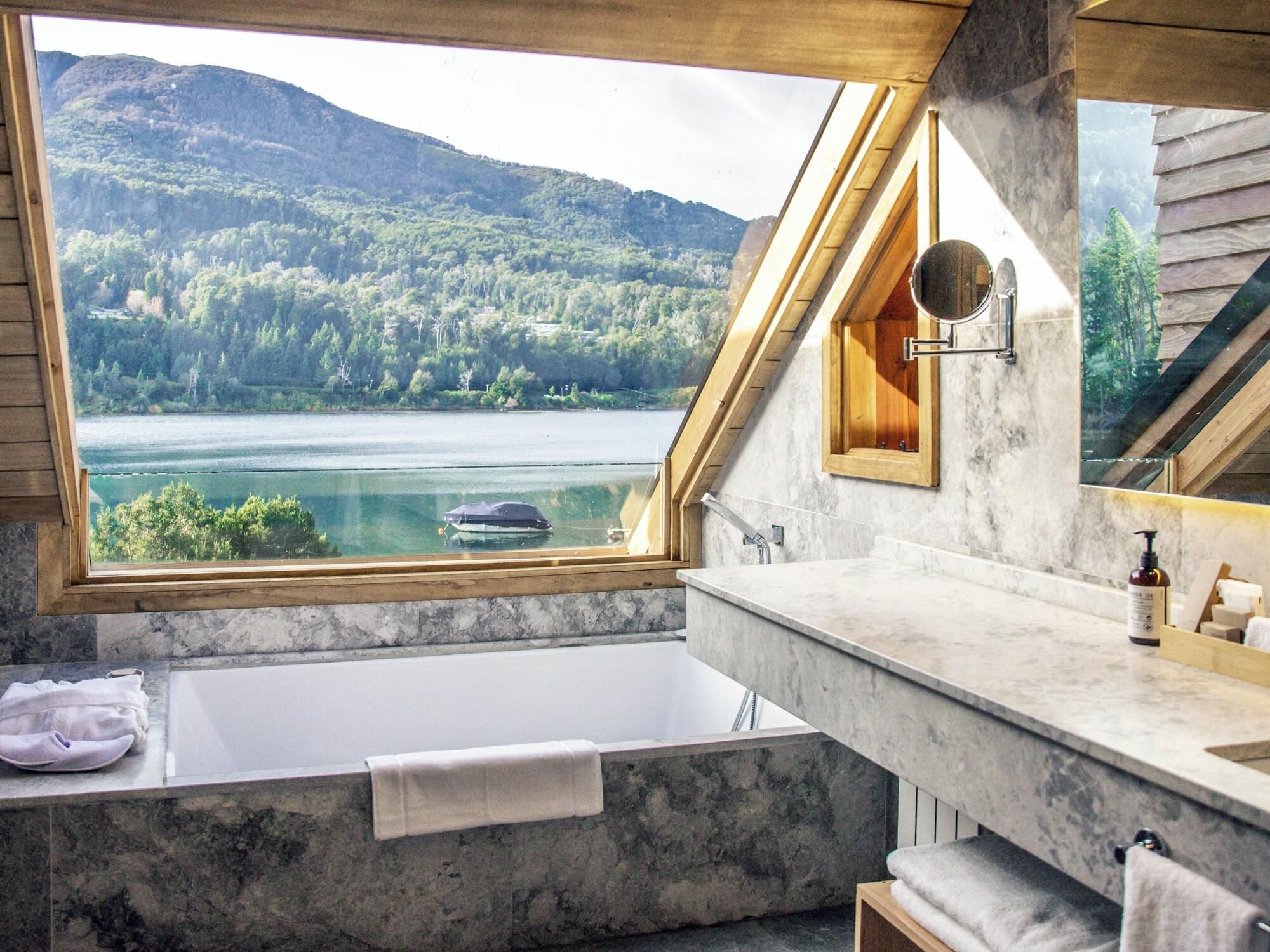 Un baño con bañera, espejo y vistas a un lago y un bosque.