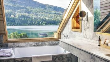 Un baño con bañera, espejo y vistas a un lago y un bosque.