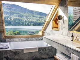 Un baño con bañera, espejo y vistas a un lago y un bosque.