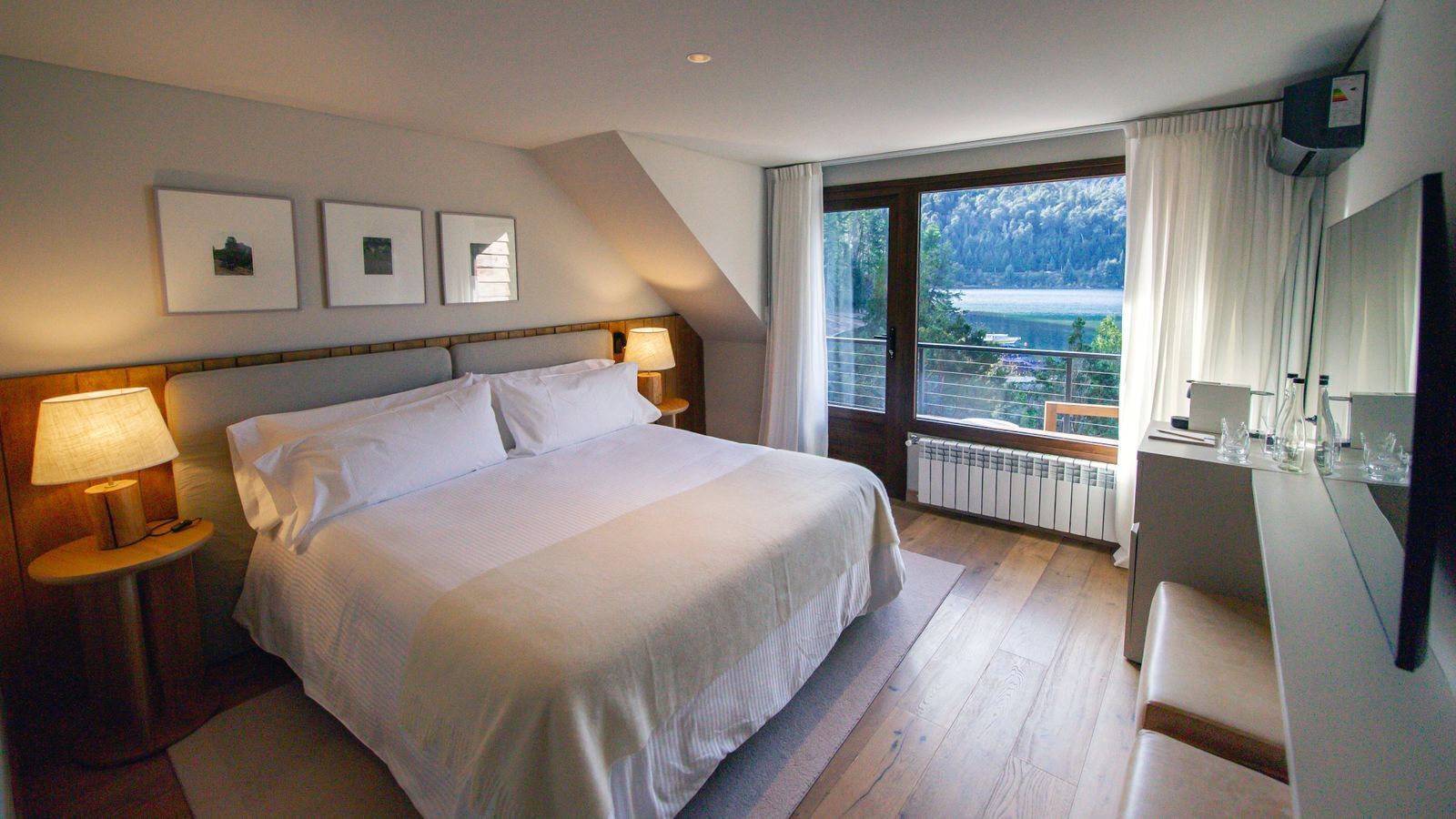 Un dormitorio con una cama grande, dos lámparas de noche, vistas a un lago y un balcón con barandilla.
