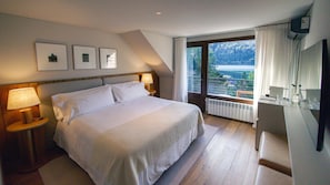 A bedroom with a large bed, two bedside lamps, a view of a lake, and a balcony with a railing. - Auria Angostura (Villa La Angostura)