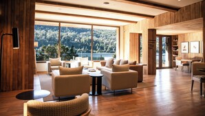 A spacious room with a large window offering a view of a forested area. There are multiple seating areas with sofas and a round table. - Auria Angostura (Villa La Angostura)