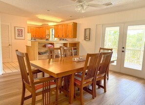 Un comedor con una mesa y sillas de madera, una cocina al fondo y un gran ventanal corredizo que da a un balcón.