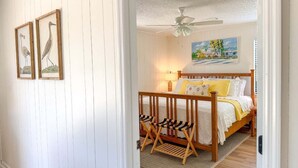 Un dormitorio con cama, barandillas de madera, ventilador de techo y cuadros en la pared.