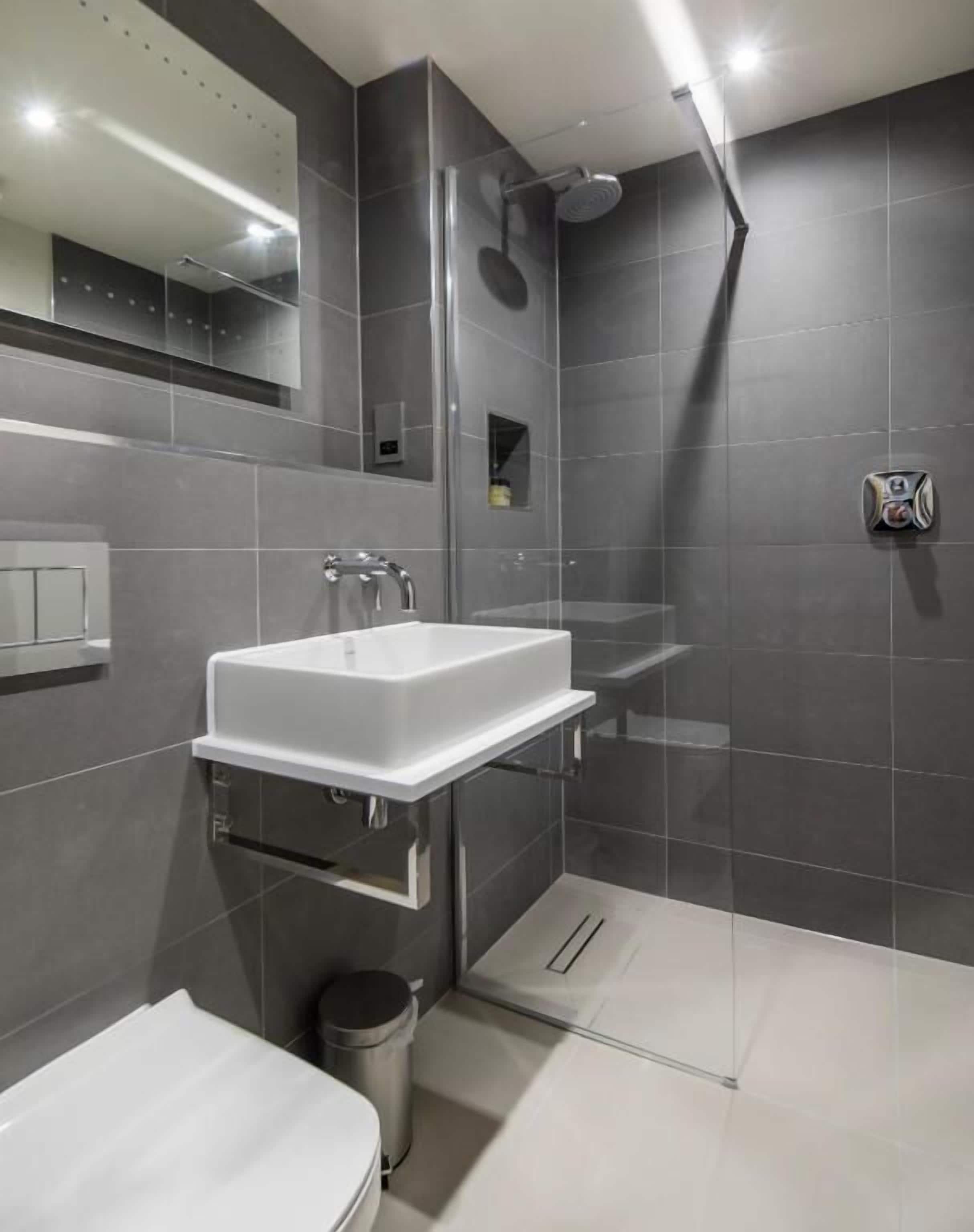 A modern bathroom with a white sink, a glass-enclosed shower, and a toilet.