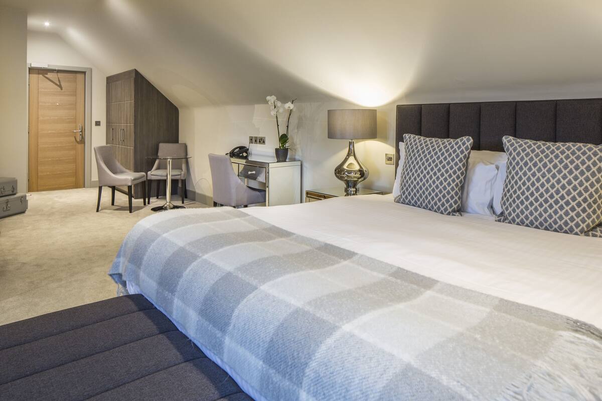A bedroom with a large bed, a desk, a chair, a wardrobe, and a lamp.