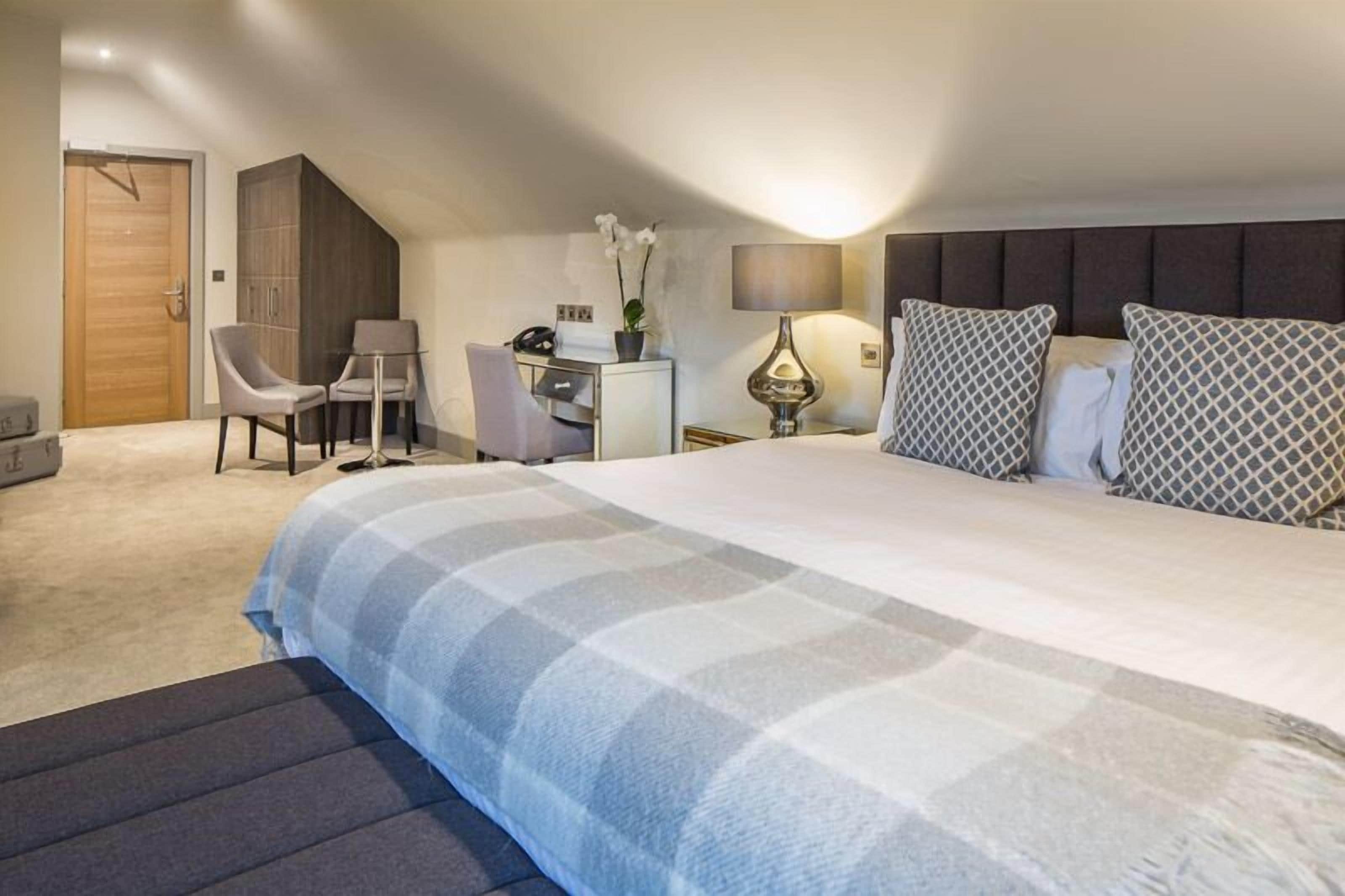 A bedroom with a large bed, a desk, a chair, a wardrobe, and a lamp.