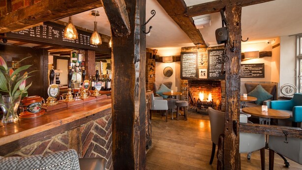 A cozy pub with a brick fireplace, wooden beams, and a bar area with taps and bottles. - The Chequers inn (High Wycombe)