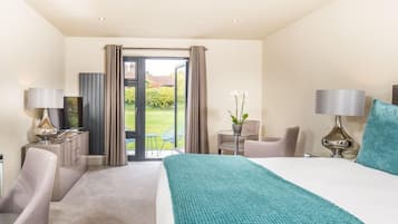 Habitación de hotel con una cama grande, dos mesitas de noche con lámparas, una silla, una pequeña mesa con una planta y vistas a un jardín a través de una puerta corredera.