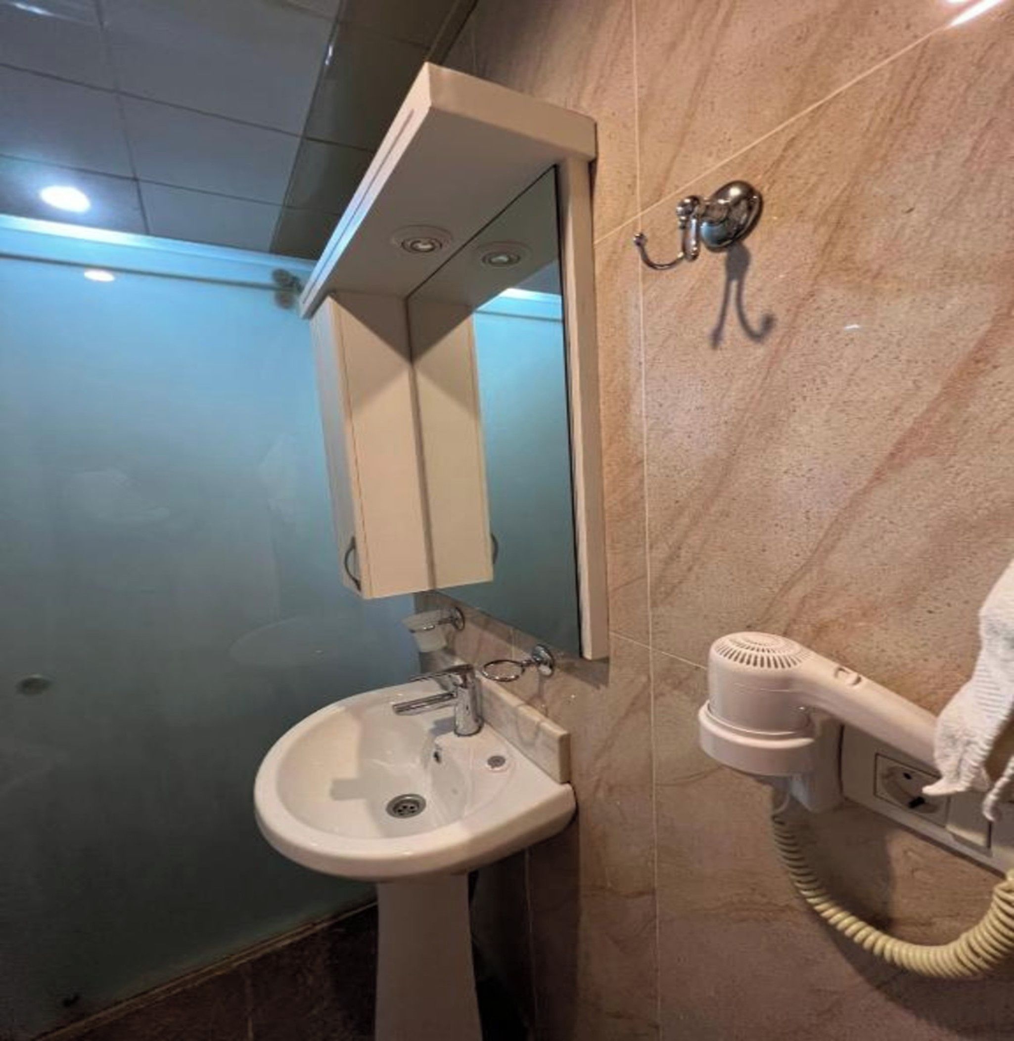 A bathroom with a pedestal sink, a mirror, and a hairdryer mounted on the wall.