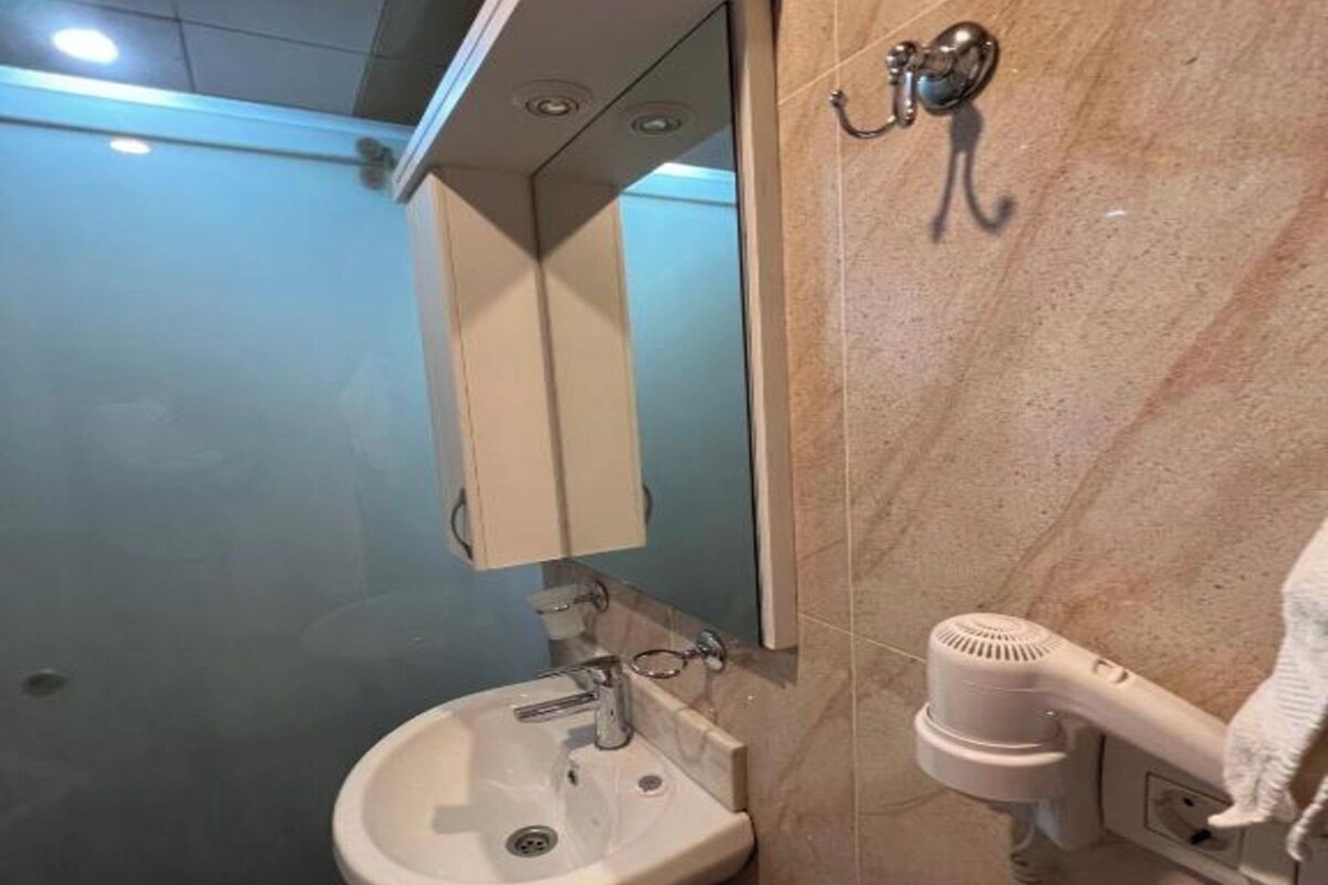 A bathroom with a pedestal sink, a mirror, and a hairdryer mounted on the wall.