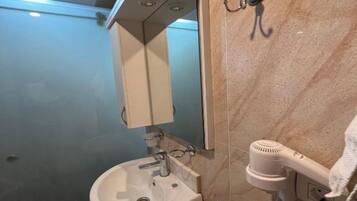 A bathroom with a pedestal sink, a mirror, and a hairdryer mounted on the wall.