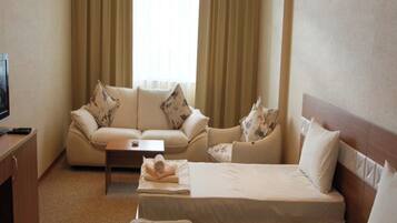 Ein Hotelzimmer mit zwei Betten, einem Sofa, einem Couchtisch und einem Fernseher.