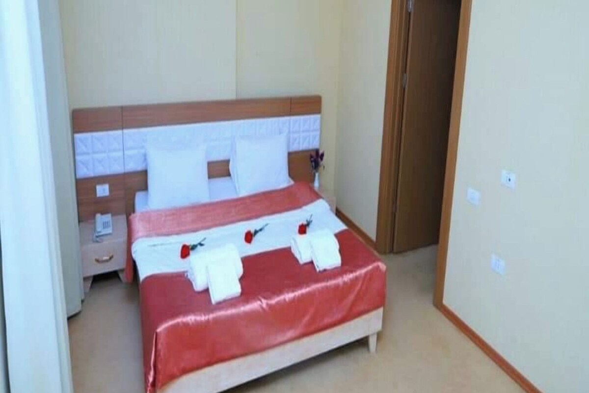 A hotel room with a bed, a nightstand, a door, and a light switch on the wall.